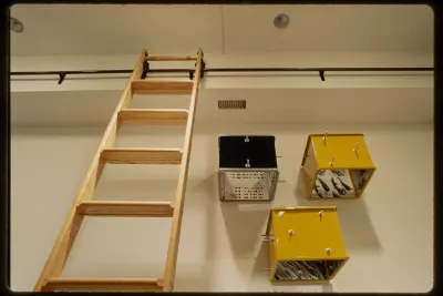 Two large wooden canvases with abstract colorful configurations are hung adjacent to five black and white comic style paintings. 