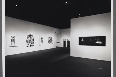 Large abstract artworks hang around the gallery space. A gallery wall stands in the center of the room.  