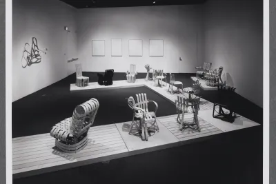 Bentwood chairs are arranged upon a wooden platform that makes its way through the gallery space. 