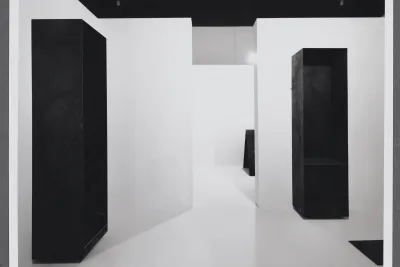 Large steel rectangular sculptures stand contrasted against white walls. Other geometric forms stand in the next space.