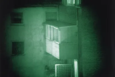 Nighttime photograph with a green hue of a porch that jets out of a building and a black vignette.