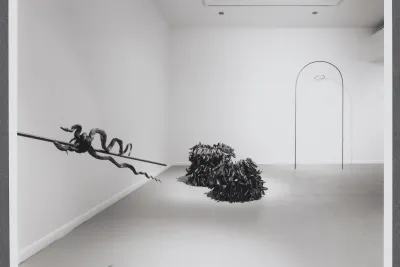 A sculpture of preserved snakes is entwined around a pole on the wall. The pole directs attention to other works in the room.