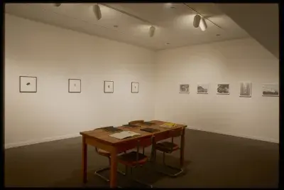 Wooden table and four metal padded chairs with six books on top sits in middle of room, nine photos of nature hang on walls.