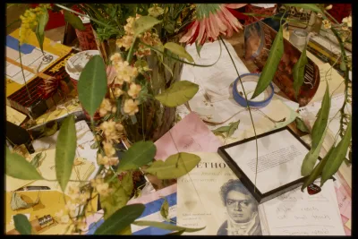 Seen from above, foliage of a floral arrangement hovers over a colorful surface strewn with stationery and other miscellany.