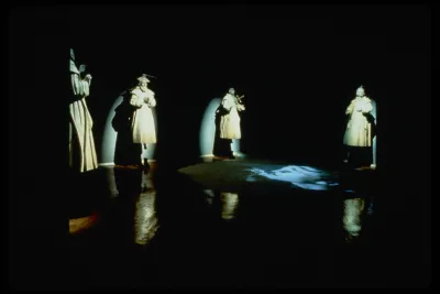 Four spotlit sculptures of saints in style of Cotan, in various pious positions with reflections and video projection on floor. 