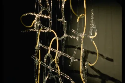 Flameworked hollow glass letters intertwined with yellowish rubber tubing, dangle from the ceiling.