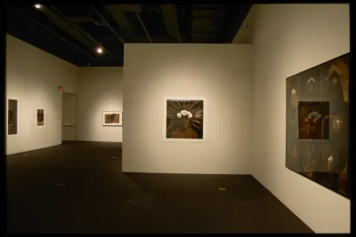 Several sepia toned photographic portraits, some punctuated with white, hang on the walls of a gallery space.