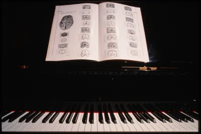 A book lies open with images of the human brain on the music rack of a black piano above a row of black and white keys.