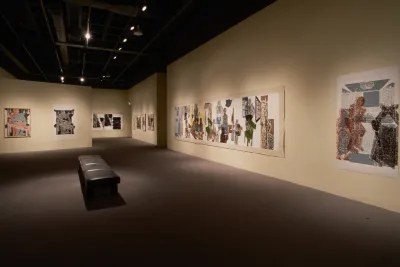 Large, muted-color woodblock prints hang on cream-color walls of a long gallery with a bench in the center for visitors