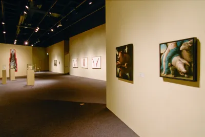2 paintings on right gallery wall lead viewer into large space displaying paintings, drawings and sculptures on pedestals.