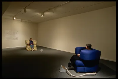 Two cushioned chairs are set across from each other. Each has large arms that squeeze the sitter between them.