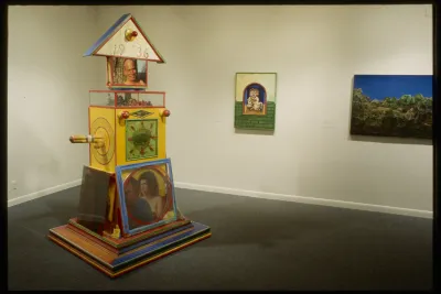 A large yellow sculpture is in the foreground with 2 paintings on the back wall of the gallery.