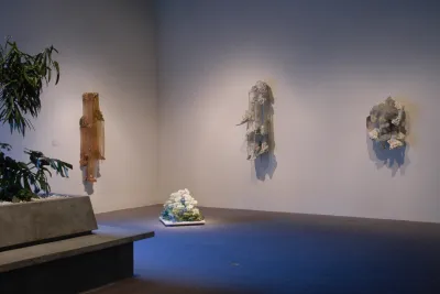 Green leaves in a bench planter point to a low floor sculpture and 3 organically-shaped sculptures hung on corner walls.