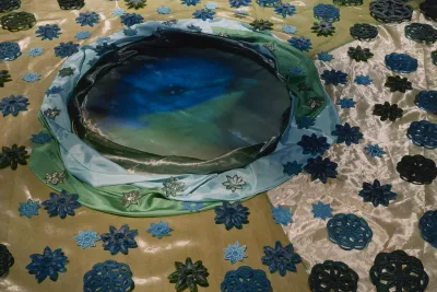 Figure under a floating canopy, projected on wall above 3 spot-lit, round installations on the floor of a dark gallery