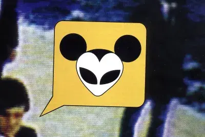 A cartoon word bubble contains a stylized Mickey Mouse with alien eyes. It sits on top of a blurred scene with 2 businessmen.