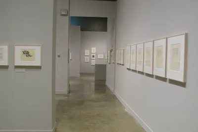 A collection of drawings framed along the walls of a divided gallery space