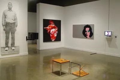 Gallery space including 2 video monitors and 3 large works mounted on the walls and small end tables centered in the room