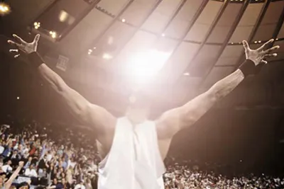 Photograph of a crowded sports arena cheering around an athlete with his arms outstretched