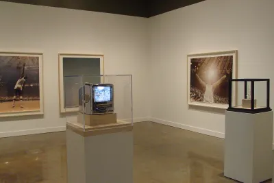 2 vitrines, with objects within, stand in front of 3 large images, framed on the walls behind