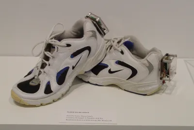 White nike sneakers with black and blue detailing and a clear box filled with electronic wires attached to each heel