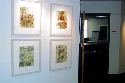 Four framed abstract artworks are hung in a grid on a wall outside of a conference room with a long table and chairs.