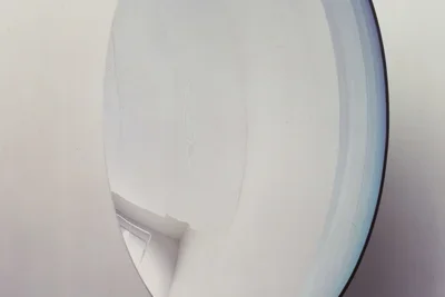 Close view of a large concave mirrored sculpture hung on a wall and reflecting the surrounding gallery space.