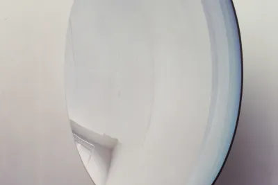 Close view of a large concave mirrored sculpture hung on a wall and reflecting the surrounding gallery space.