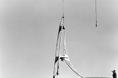 An image depicts the installation of a sculpture atop the MIT Bell Tower. A crane lowers it while onlookers help its placement.