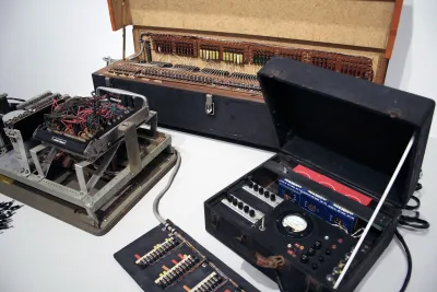 Close up photo of several vintage electronic objects displayed on a white pedestal.
