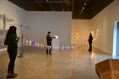 Two people in a gallery hold a colorful garland and a third person looks at the garland.