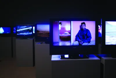 Many screens installed on podiums in a darkened gallery.
