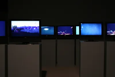 Many screens installed on podiums in a darkened gallery.