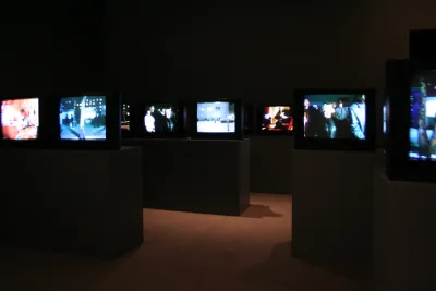 Many screens installed on podiums in a darkened gallery.