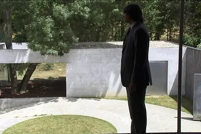 A man in a suit standing in a park like setting.