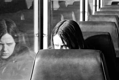 A girl on the bus looks at her own reflection in the window and is obscured by the seat in front of her.