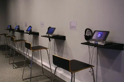 A wall of small TVs with individual headphones installed in a gallery.