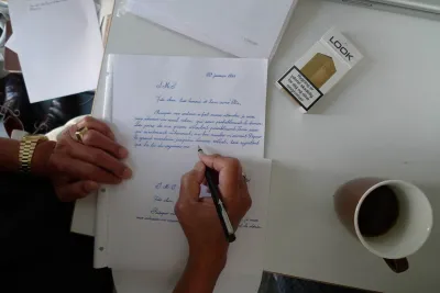 A hand writing and a letter are in frame.