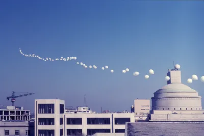 A skyline photo of buildings at MIT, a clear blue sky and a string of large white weather balloons floating into the distance.