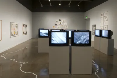 Installation showing many TV monitors and art on the surrounding walls.