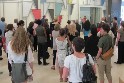 Gallery visitors stand around a wall bound artwork by Martin Boyce featuring colorful steel trianges.
