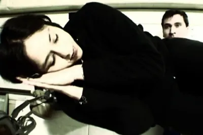 A single frame with a woman lying on her side, eyes closed, hands under her head, a man standing behind her