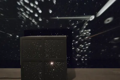 A large black square rests on the floor with light emanating from within.