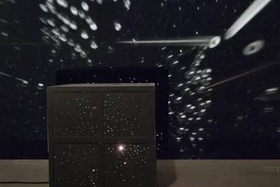 A large black square rests on the floor with light emanating from within.