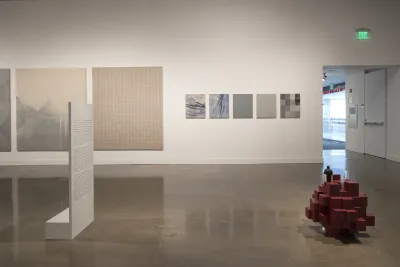 View of gallery with multipanel paintings in the back and red brick sculpture on the ground.