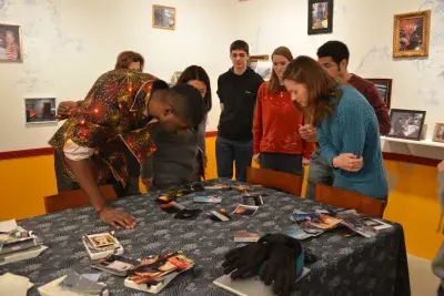 Students gather near the corner of a table and look at printed photos on the table.
