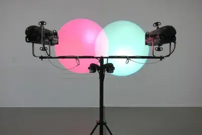 Two lamps on a stand, both at equal height, cast a pink and a green circle of light which overlap one another in the center.