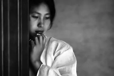 Muted mage of a young korean woman, in draped white clothing, cheek and hand resting against a wall, eyes cast down.