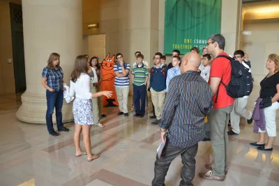 A crowd gathers around a woman who is giving a talk.