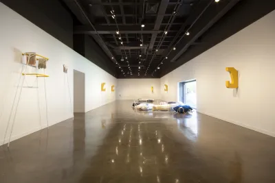 Closeup of a wall-mounted cast aluminum sculpture, hook shaped and painted yellow.