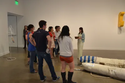 People attend a gallery talk with a guide and gather near a soft, floorbound sculpture.